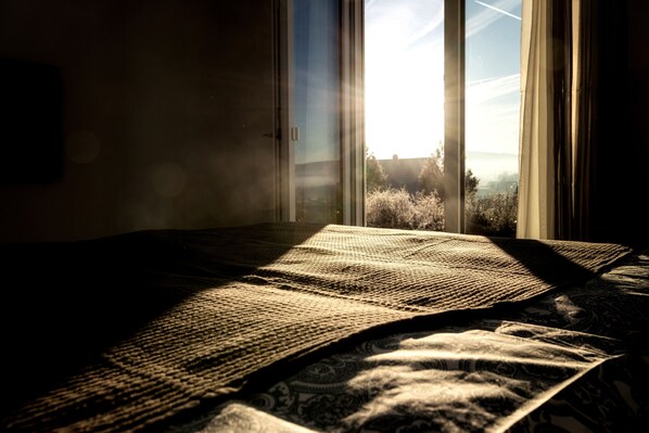 Una cama con una colcha estampada y vistas a un paisaje a través de una ventana.