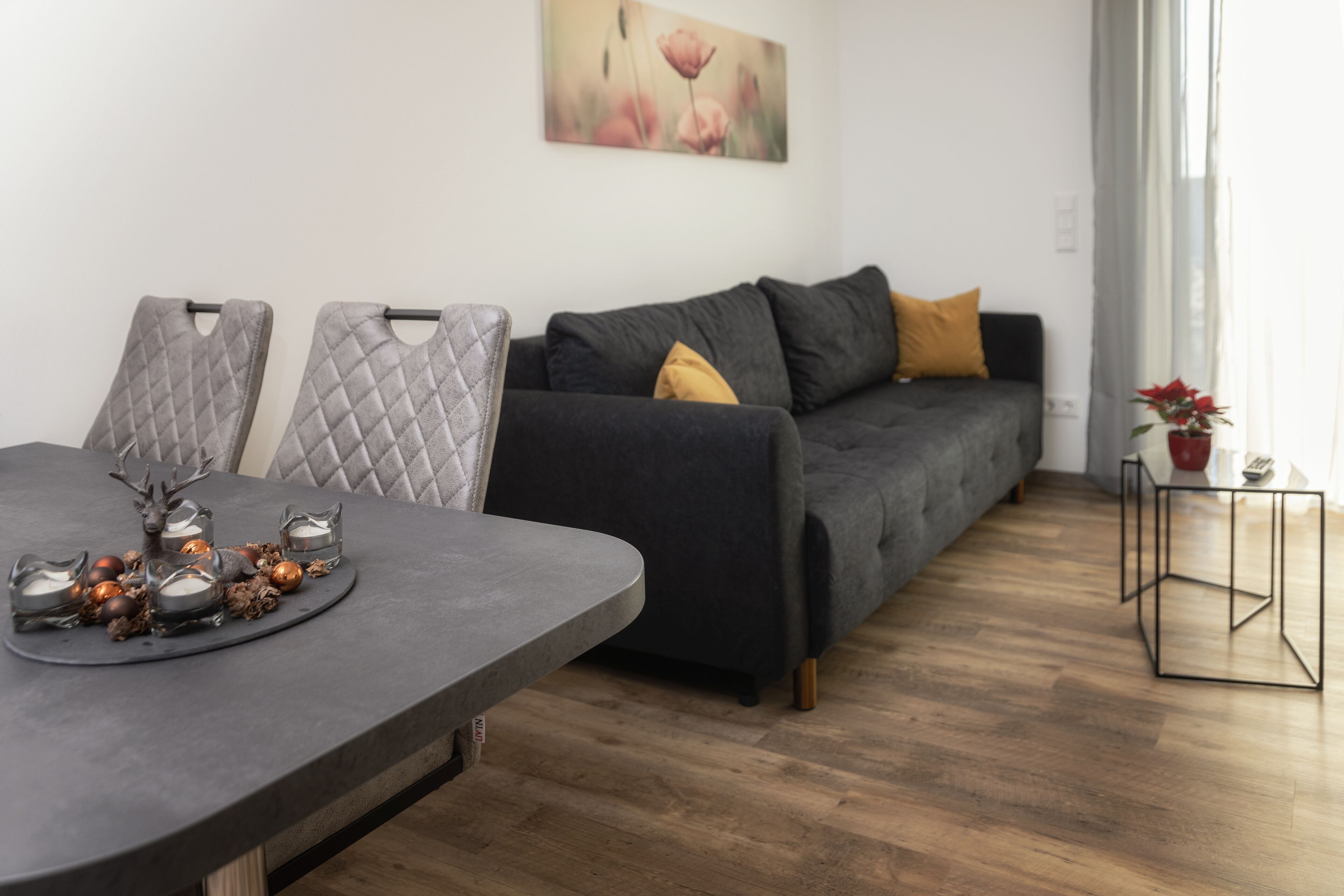 Ein modernes Wohnzimmer mit einem dunkelgrauen Sofa, einem runden Esstisch mit dekorativer Dekoration und einem schlichten Couchtisch.