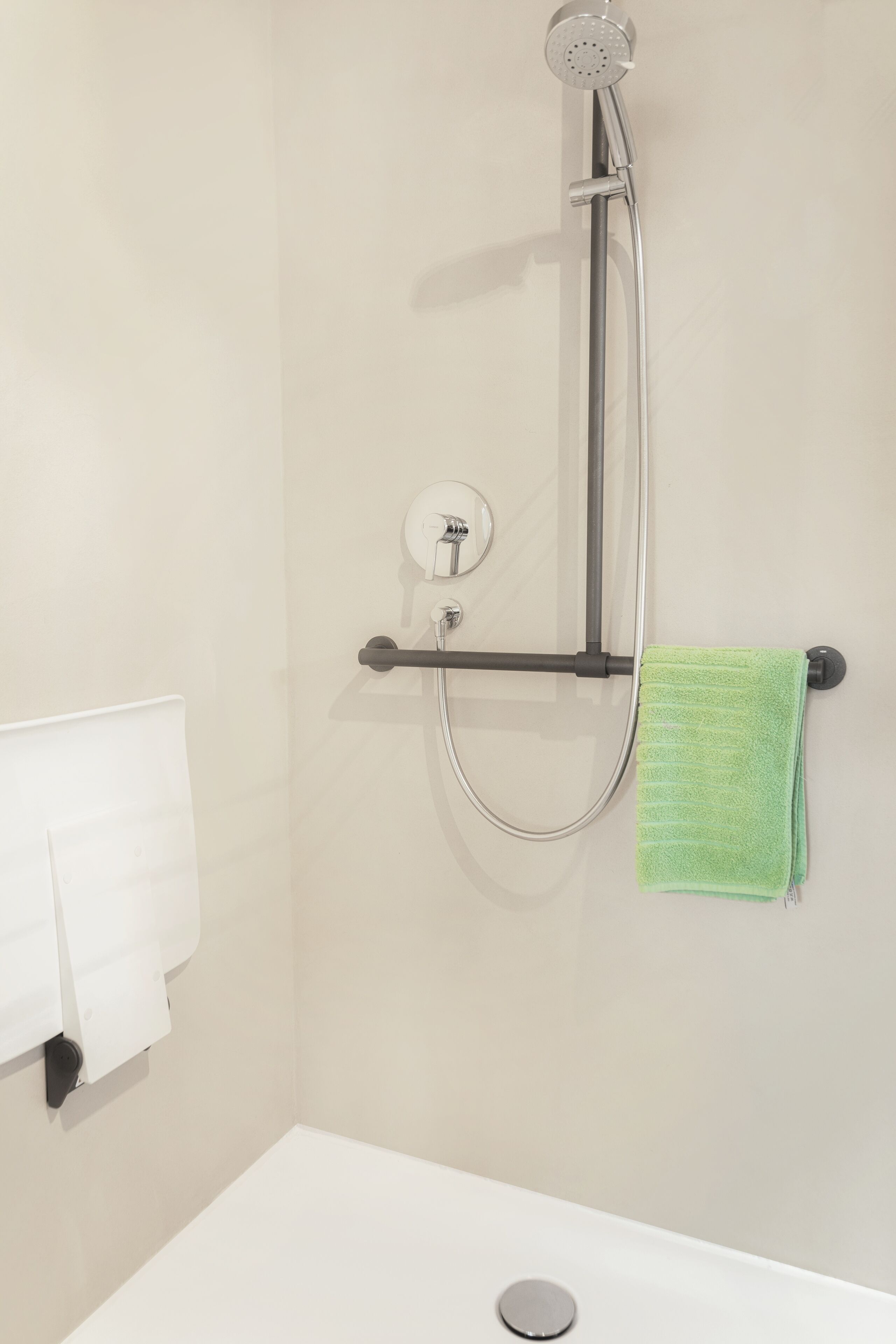 Un baño con ducha, un perchero y una toalla verde, además de una toalla blanca en un soporte de pared.