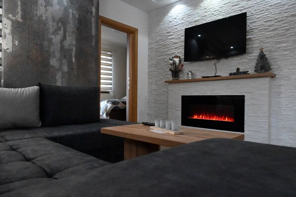A modern living room with a gray sofa, a wooden coffee table, a fireplace, and a mounted TV.