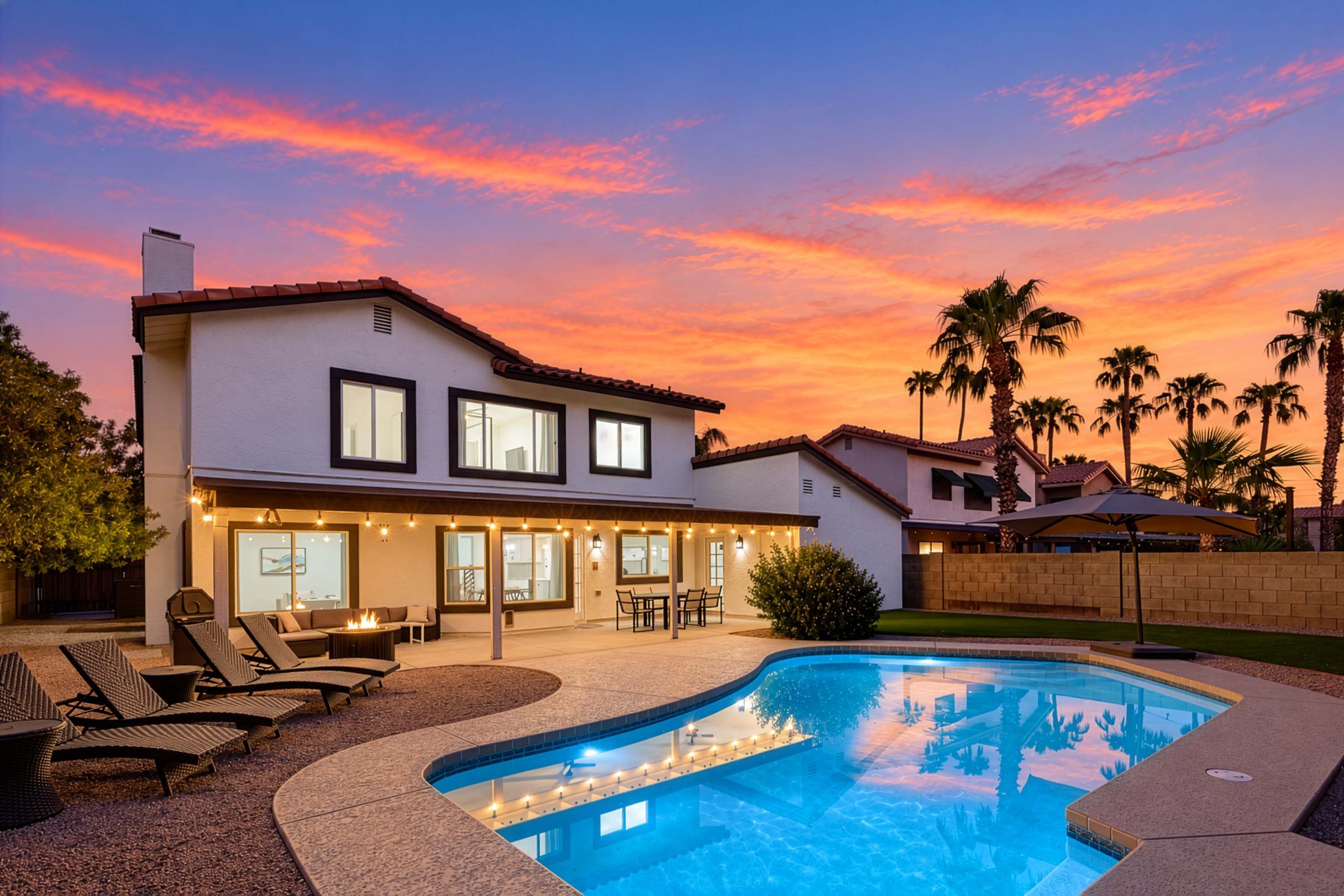 A two-story house with a swimming pool, outdoor seating, and a sunset sky.