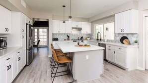 A modern kitchen with white cabinetry, a central island with bar stools, stainless steel appliances, and pendant lighting. - Sereno- North Scottsdale- Private Pool & Games! (Scottsdale)