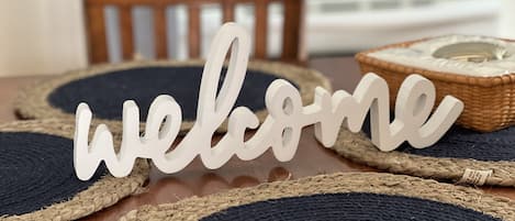 Une table à manger en bois, agrémentée de sets de table en fibres tressées et d’une pancarte indiquant « Bienvenue ».