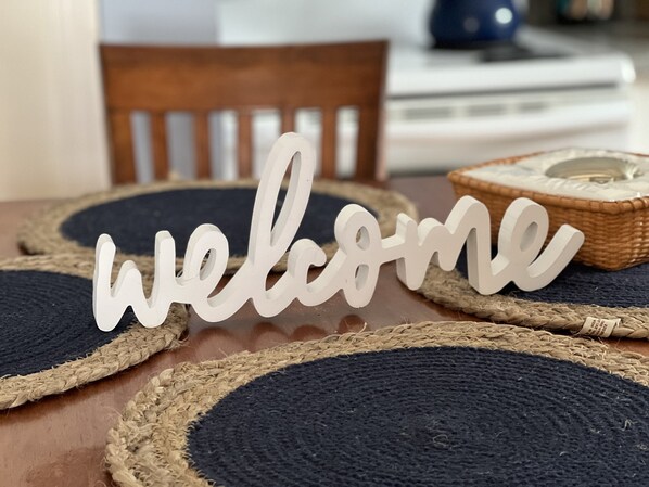 A wooden dining table with woven placemats and a 'welcome' sign.
