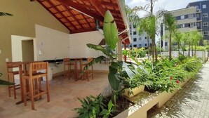 An outdoor patio area with wooden chairs and tables, surrounded by planters with various plants and flowers.