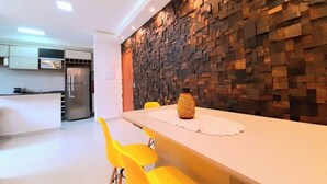 A modern kitchen with a stone backsplash, a dining area with yellow chairs, and a white table.
