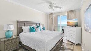 Ein Schlafzimmer mit Bett, Nachttisch, Lampe, Kommode, Fernseher und Meerblick.