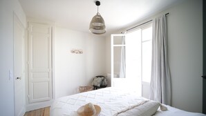 A bedroom with a bed, a hanging light fixture, a window with curtains, and a door. - Villa 1900 "Jeanne", fully renovated, 100 meters from the beach (Le Tréport)