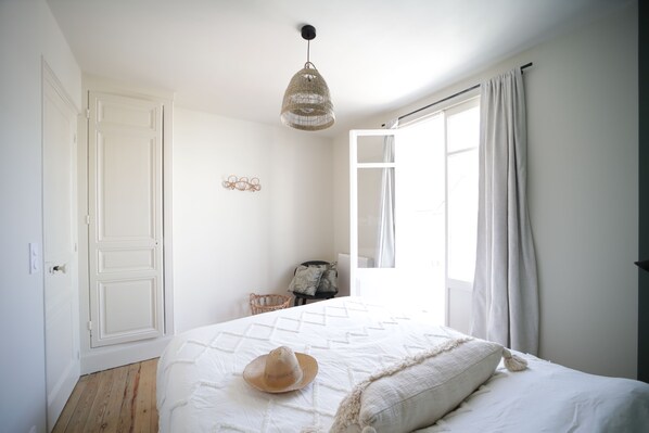 A bedroom with a bed, a hanging light fixture, a window with curtains, and a door.