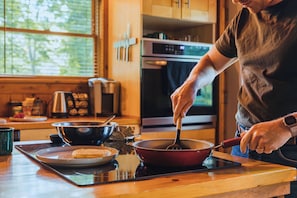 A person cooking in a kitchen with a stove, pots, and a window.