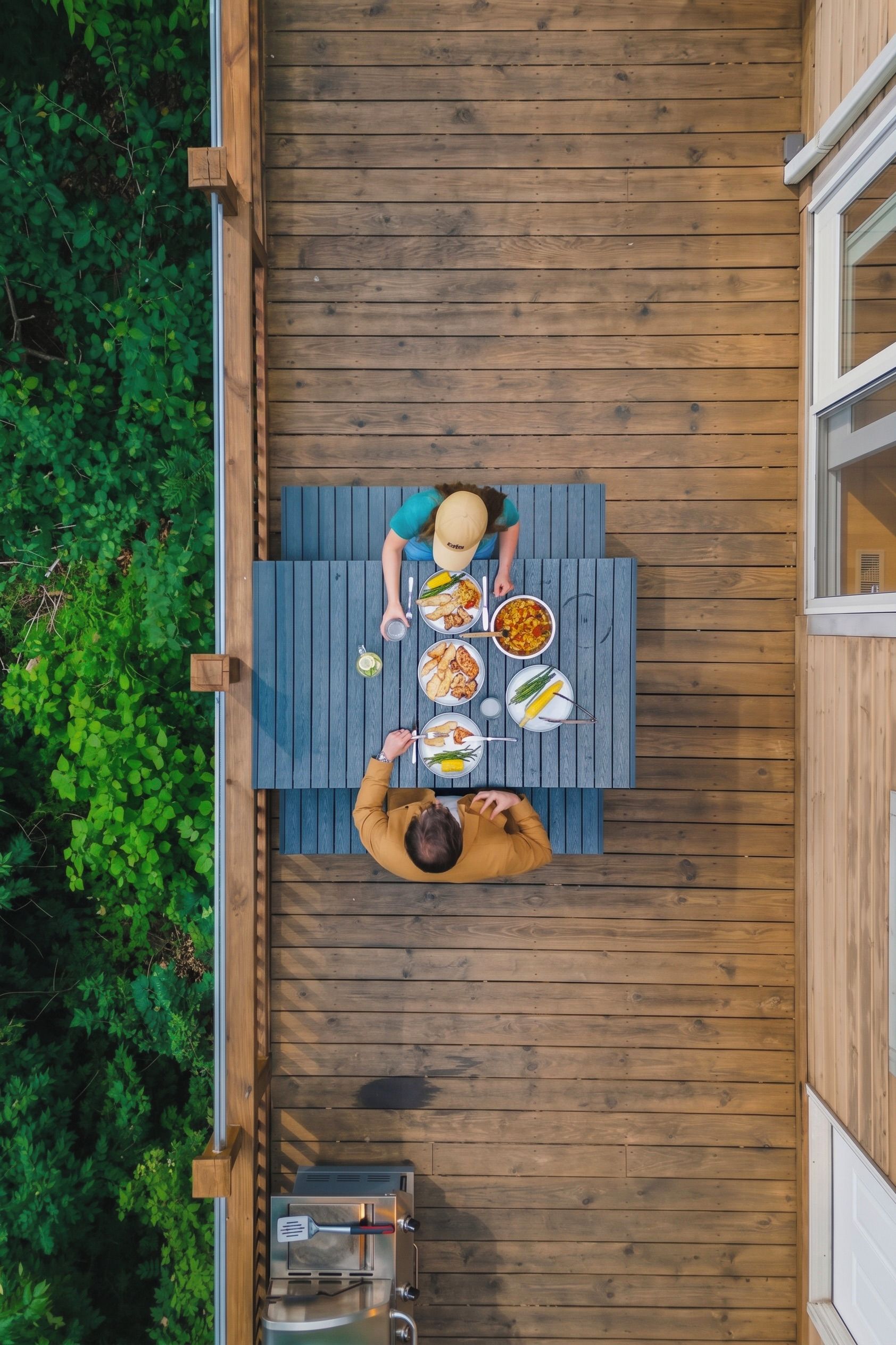 A wooden deck with a table set for two people, surrounded by greenery.