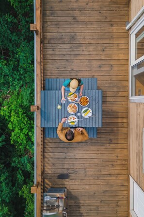 A wooden deck with a table set for two people, surrounded by greenery.