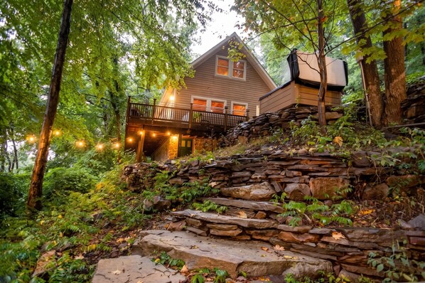 A house with a stone staircase leading to a wooden deck with string lights.