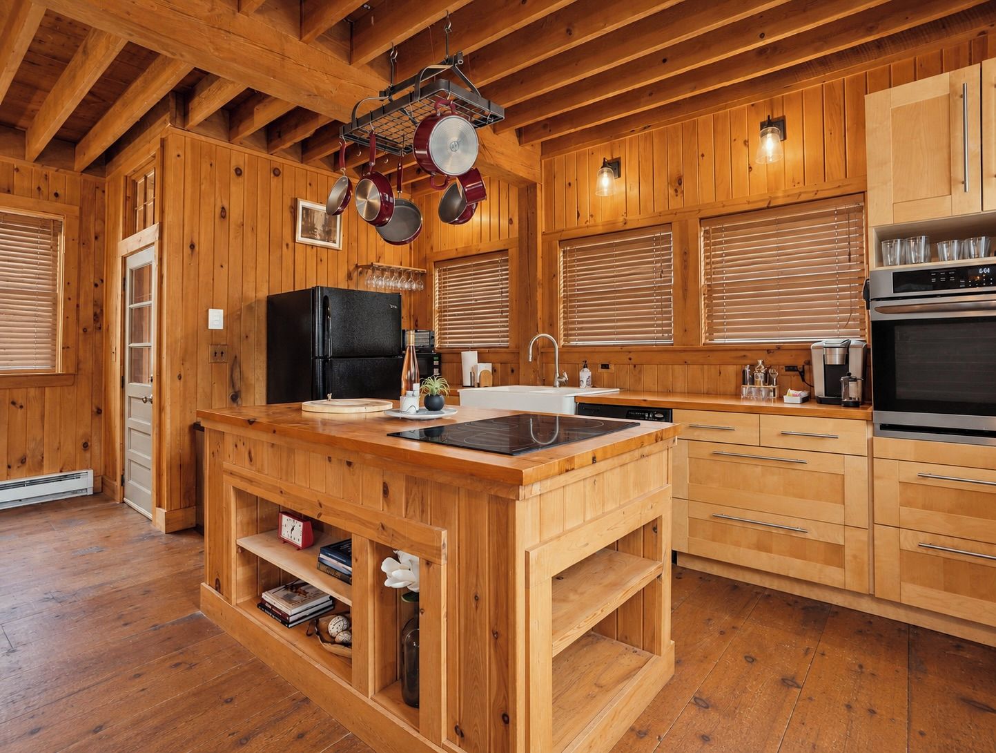 Une cuisine de style rustique, avec des éléments en bois, un îlot central, des appareils électroménagers intégrés et un porte-casseroles suspendu.