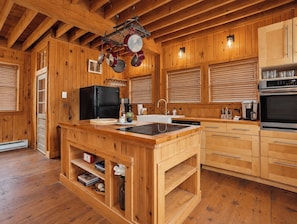 A wooden cabin-style kitchen with a central island, built-in appliances, and a hanging pot rack.