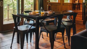 A wooden cabin with a dining table set for four, large windows, and a view of trees outside.
