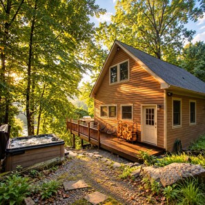 A cabin with a deck, a hot tub, and a view of the surrounding forest.