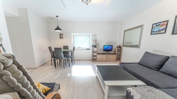 Una sala de estar moderna con un sofá, una mesa de centro, un comedor con una mesa y sillas, un televisor y una ventana.