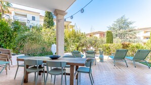 An outdoor patio with a wooden table and chairs, surrounded by greenery and a clear sky.