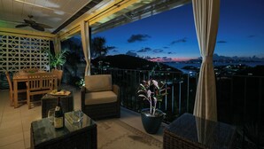 Ein Balkon mit Korbmöbeln, einem Topfpflanzen und Blick auf eine Stadtlandschaft im Abenddämmerung.