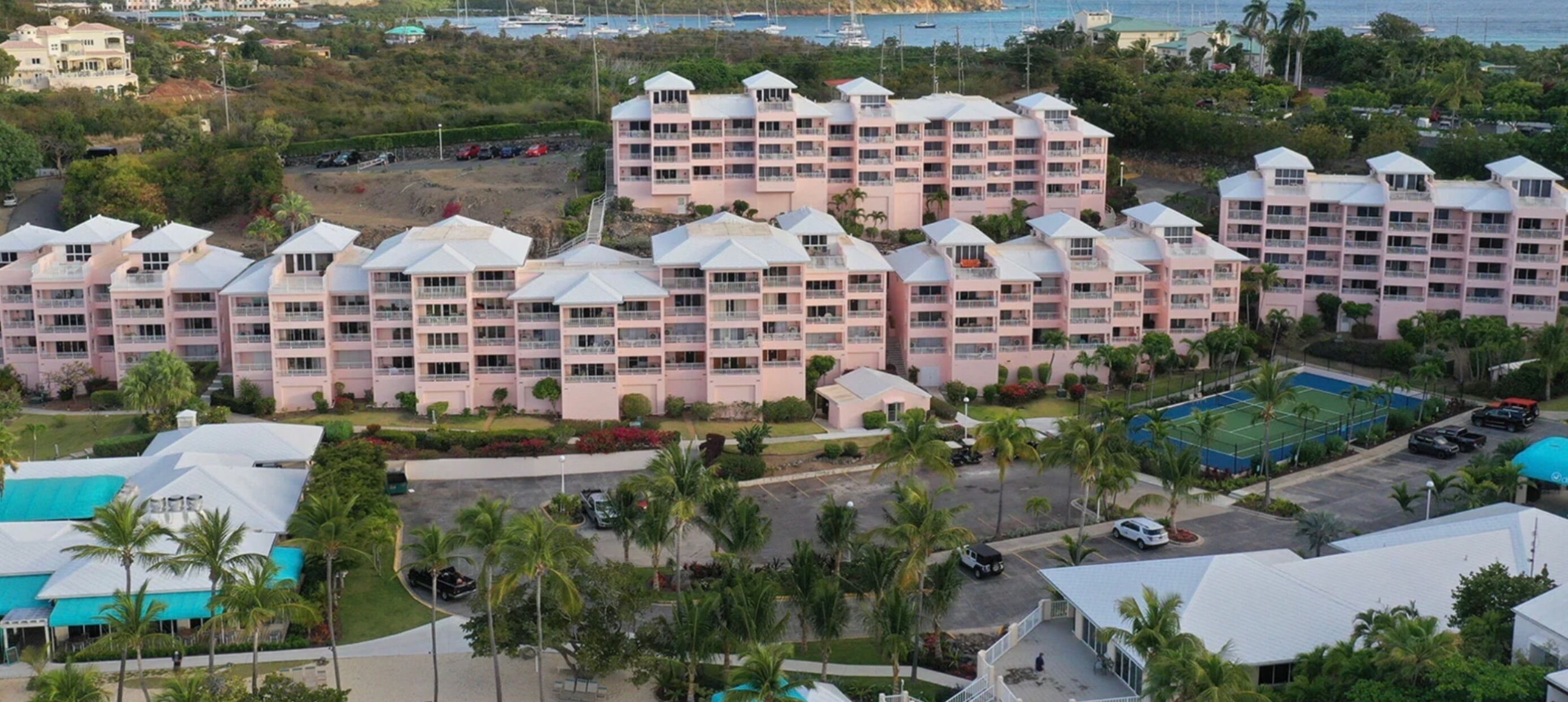 A multi-story hotel with balconies, a swimming pool, and a marina in the background.