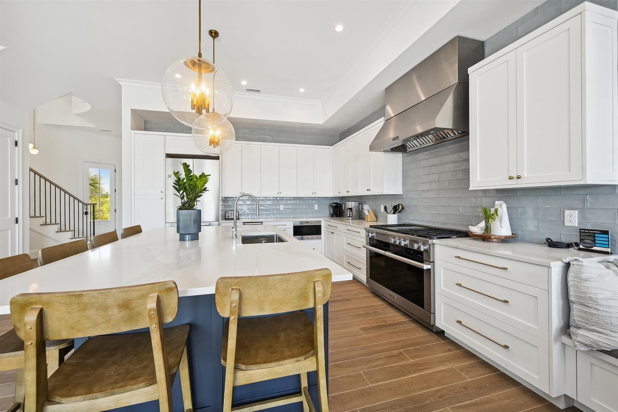 Een moderne keuken met witte kasten, een centraal eiland met barkrukken, een roestvrijstalen afzuigkap en een hangende hanglamp.
