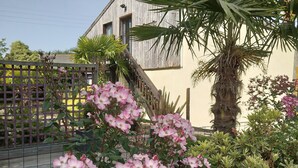 A garden with pink flowers, a palm tree, and a building in the background. - Quiet 1st floor apartment with balcony and patio, 18 km from the sea (Landebia frankreich)