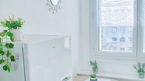 Een functionele keuken met een witte koelkast, een tafeltje met stoel en een raam met uitzicht op gebouwen.
