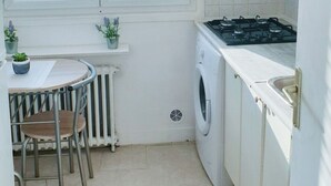Een compacte keuken met een fornuis, wasmachine en een klein eethoekje met een tafel en stoelen.