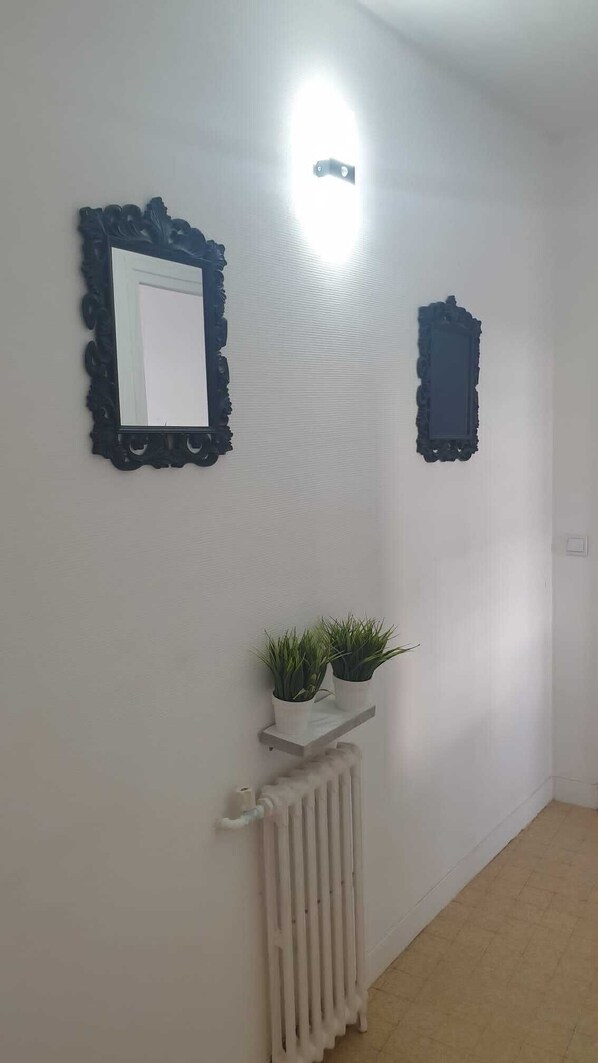 A hallway with a radiator, a light fixture, and two wall-mounted mirrors.
