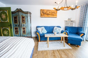 A room with a blue sofa, a wooden table, a green door with floral decorations, and a painting on the wall.