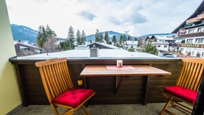 Un balcon avec deux chaises en bois et une table, donnant sur un paysage montagneux.