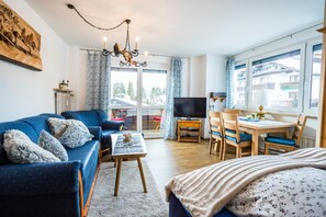 A modern living room with a sofa, a coffee table, a TV, and a dining area with chairs and a table. - Beautiful family apartment near the golf course Amalie by MoniCare (Seefeld in Tirol)