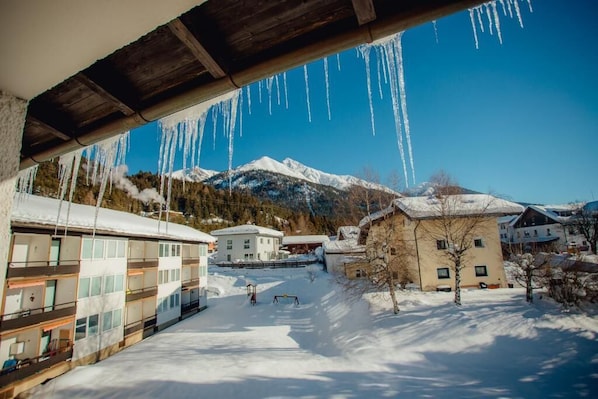 A snowy mountain village with buildings under a wooden bridge.