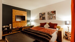 Een moderne hotelkamer met een houten accentmuur, een flatscreen televisie, een bed met rode beddengoed, twee nachtkastjes met lampen en kunstwerken aan de muren.