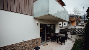 Een modern huis met een glazen balkon, een stenen basis en een terras met tuinmeubilair.