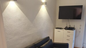 Een woonkamer met een zwarte leren bank, een flatscreen-televisie aan de muur en een wit dressoir met lades.