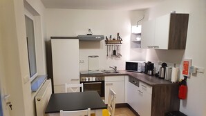 Een compacte keuken met witte kastjes, een fornuis, magnetron en een klein eethoekje met een tafel en stoelen.