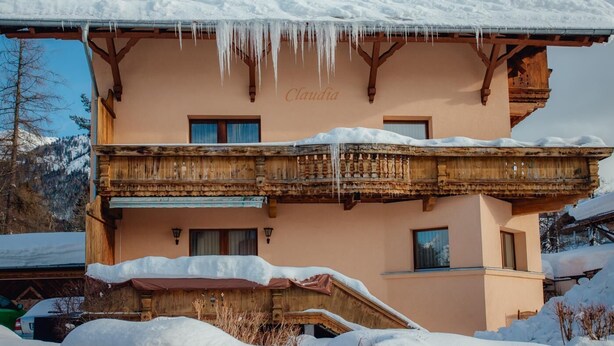 Een gebouw met twee verdiepingen, een balkon, een met sneeuw bedekte sneeuwkap en een bordje met de tekst 'Claudia'.