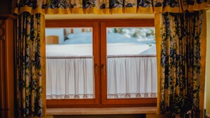 Een kamer met een houten raamkozijn, witte gordijnen met kantbies en een gebloemd valances.