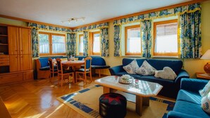 Een ruime woonkamer met een blauwe bank, een eettafel met stoelen, en een keuken met houten kasten.