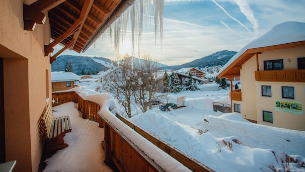 Un balcón cubierto de nieve con barandas de madera y vista a un pueblo nevado y montañas.