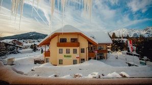 Un hotel de varios pisos con tejado nevado, rodeado por un paisaje invernal y montañas.