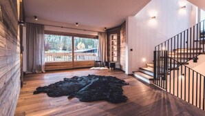 Um quarto espaçoso com piso de madeira amplo, tapete preto, escada com corrimão preto e vista para um deck através de uma grande janela.