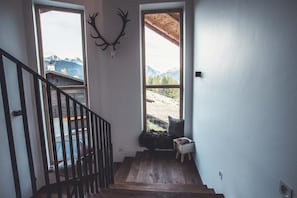 A staircase with wooden steps leading to a balcony, a mounted deer skull on the wall, and a view of mountains through large windows.
