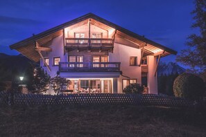A two-story chalet with a balcony, wooden exterior, and a well-lit entrance. - Alpine chic in Haus Hahn, combined with modern elegance Chalet Seefelder Spitze by MoniCare (Seefeld in Tirol)