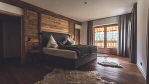 Quarto moderno com cabeceira de madeira, uma cama grande com almofadas, tapete de pele e vista para um deck de madeira através de uma porta de correr de vidro.