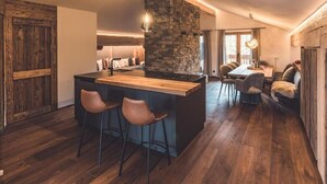 Uma cozinha moderna com uma ilha central, banquetas de bar e uma parede decorada com pedra.