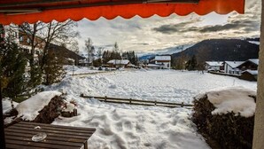 Ein verschneiter Außenbereich mit einer Holzbank und einem Metalltisch, umgeben von schneebedecktem Boden und einem Holzzaun.