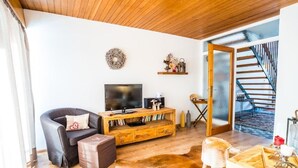 Ein Wohnzimmer mit Holzboden, einem schwarzen Ledersofa, einer Holz-TV-Bank und einer Treppe, die zu einer oberen Etage führt.